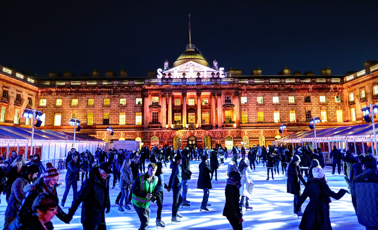 People skating on a crowded ice skating rink in Somerset House in the evening.