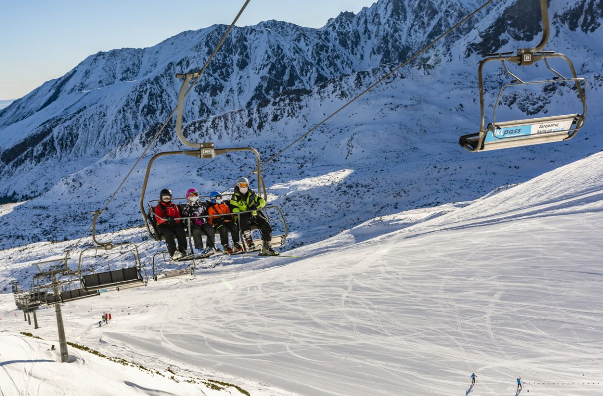 Zakopane, Poland - March 02, 2021: Recreational skiing during the Covid-19 pandemic. A family of skiers wearing protective masks going by chairlift to the top of Kasprowy Wierch. Tatra Mountains.