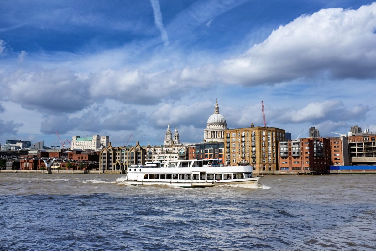 Pleasure boat sailing down the Thames River, London. The Millennium Bridge and St Paul's Cathedral can be seen in the background. Summer day with blue sky and puffy clouds.