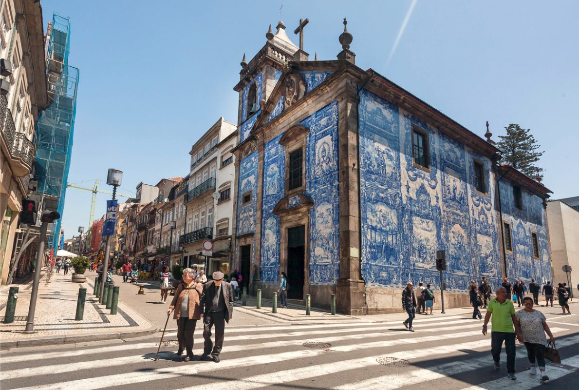 Porto, Portugal:  Elderly people walking past historical buildings with blue ceramic tiles azulejo on 22 May, 2019. Portuguese language has 250 million total speakers