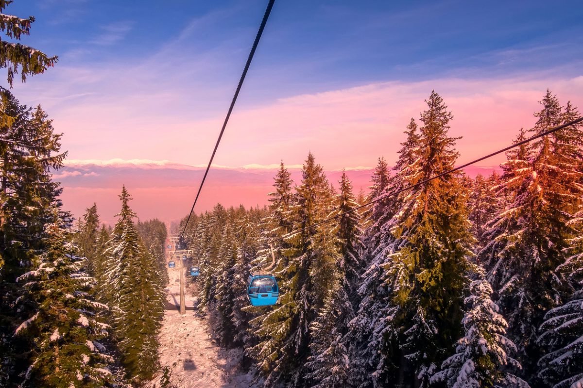Bansko, Bulgaria winter ski resort pink sunset view, lift cabins, pine trees and snow mountain peaks