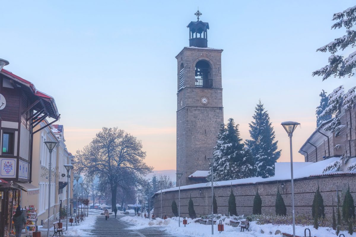 Bansko, Bulgaria - December 6, 2019: Pirin street in old town, bell tower and wall of Sveta Troitsa Church