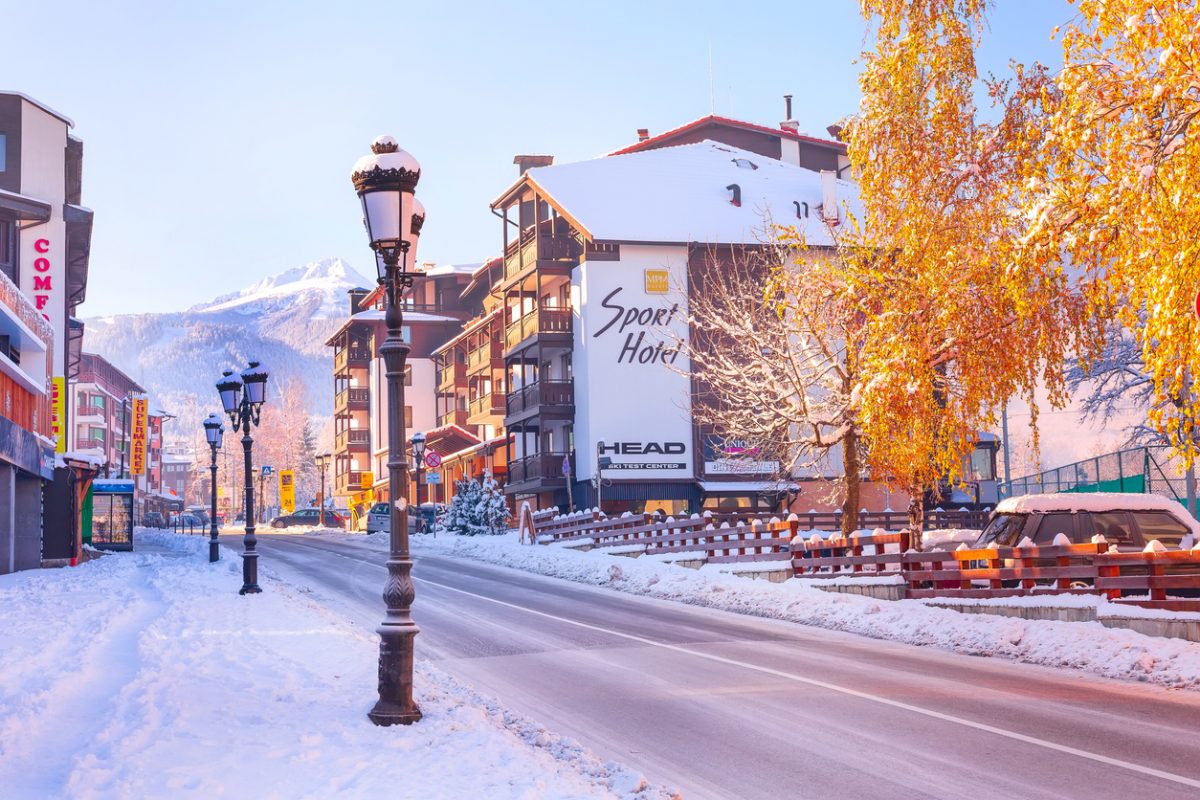 Bansko, Bulgaria - December 5, 2019: Pirin street view, Sport hotel and Todorka snow mountain peak and yellow tree
