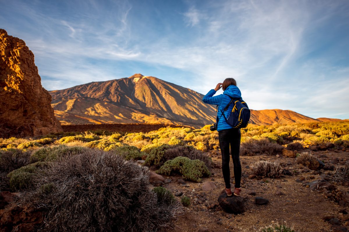 Young female traveler with bacpack standing on the stone and looking forward in Teide park on Tenerife island