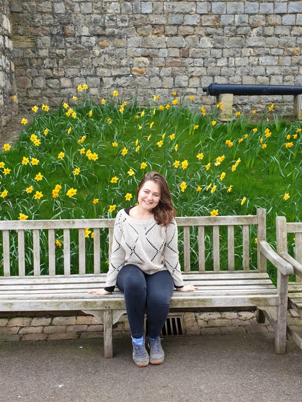 Girl sitting on bench in Windsor in February with daffodils in the background. 