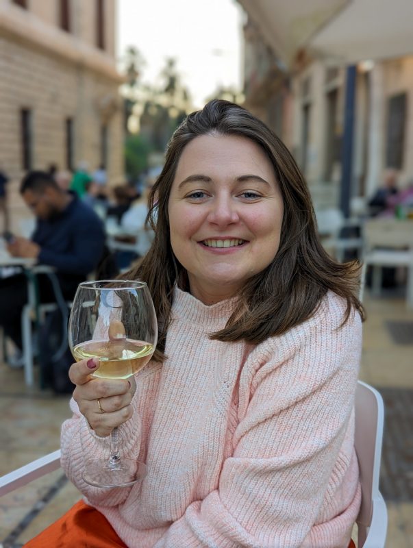 Girl enjoying a glass of wine wearing a light pink jumper with roads in the background in Malaga in winter. 