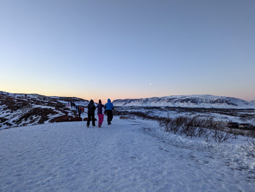 Three people walking toward the Kerid Crater in thick snow.