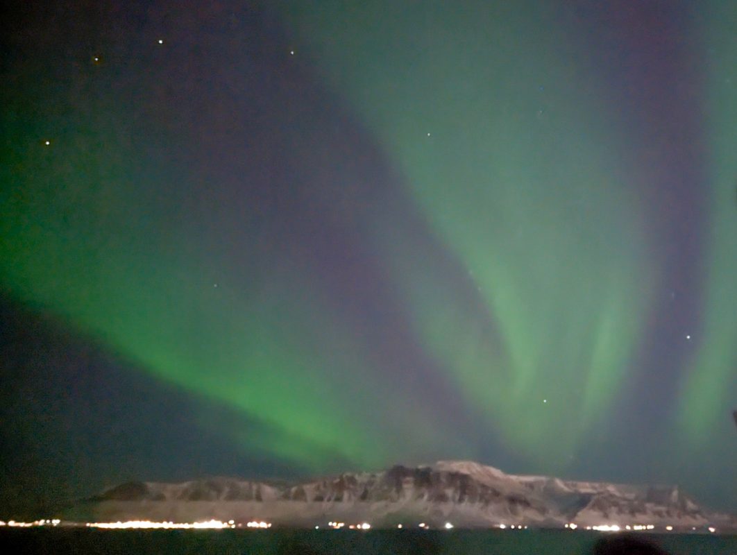 Northern Lights behind snow-capped mountains on a Reykjavik boat tour.