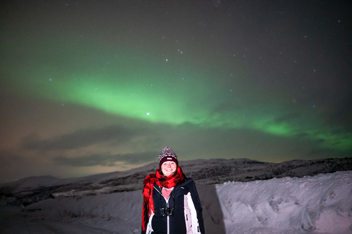 Girl standing in front of the northern lights in a snowy landscape in Norway, near the border with Finland