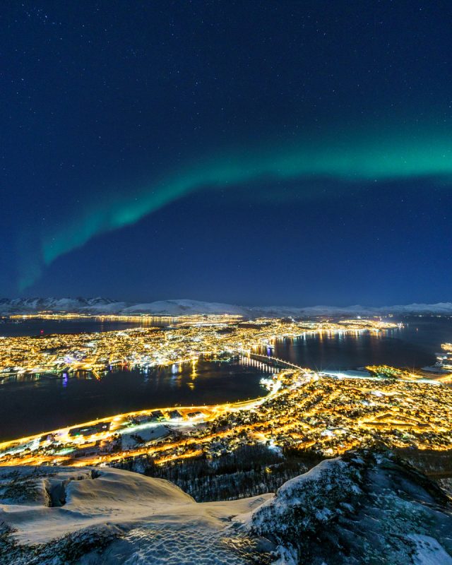 View of the twinkling city beneath the arched northern lights