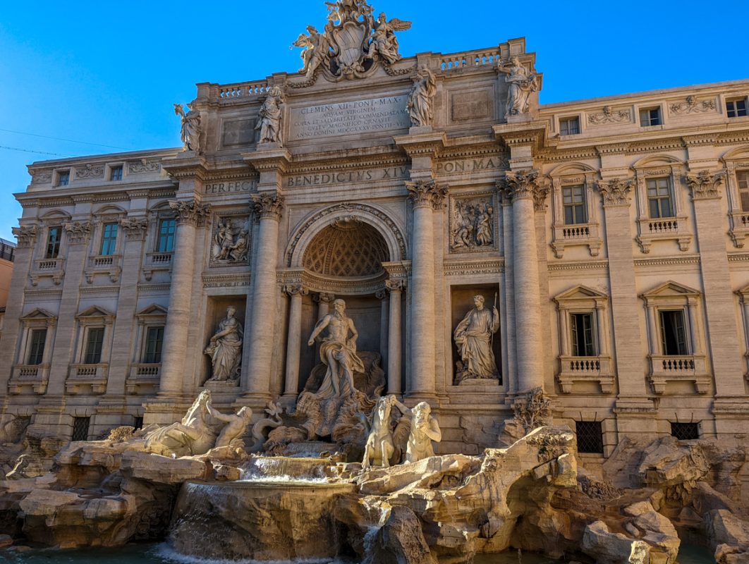 A photo of the Trevi Fountain, showcasing its intricate baroque architecture and stunning details. Water cascades from the central figure of the fountain, surrounded by sculptures and ornate carvings.