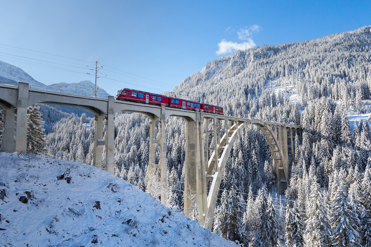 Langwieser Viaduct in winter with red Rhaetian railway train on viaduct Langwies, sunshine, winter, snow, blue sky Langwies, Switzerland.