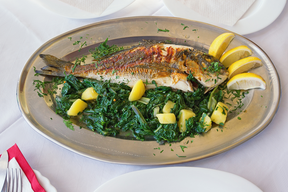 Balkan cuisine. Grilled fish (sea bream) with green leafy vegetables and lemon slices