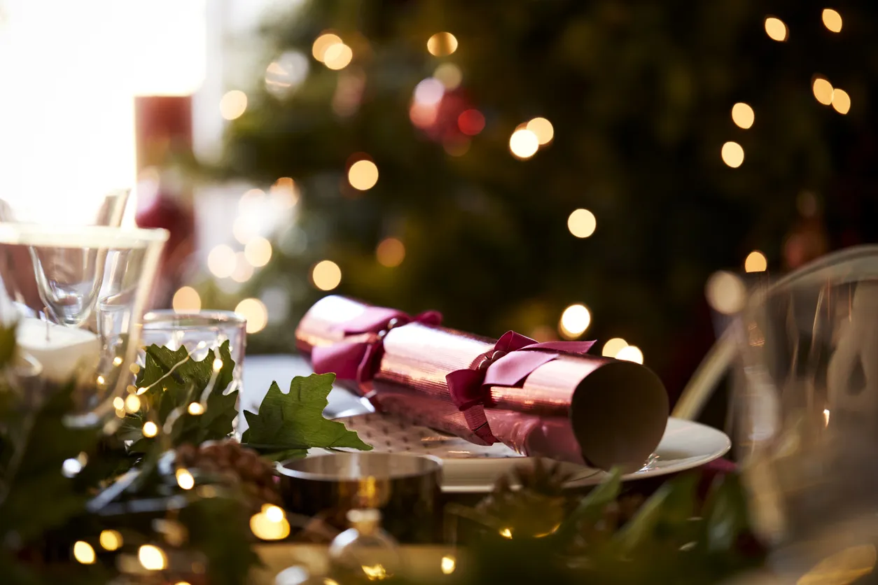 Close up of Christmas table setting with a Christmas cracker arranged on a plate and Christmas tree in the background