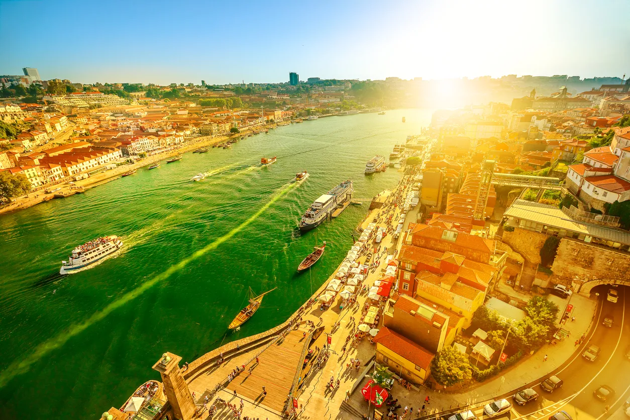 Aerial view of Oporto skyline and Ribeira Waterfront from Dom Luis I Bridge at twilight. Picturesque urban cityscape of Porto in Portugal. Tourist boats cruising on Douro River at sunset light.