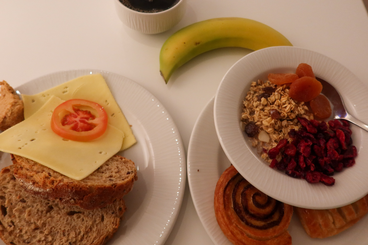 Bread, cheese and tomato with museli in another bowl and a banana and coffee.