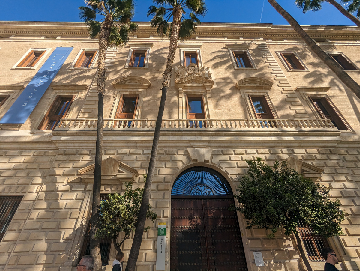 The outside of the museum of Malaga, with palm trees in the foreground.