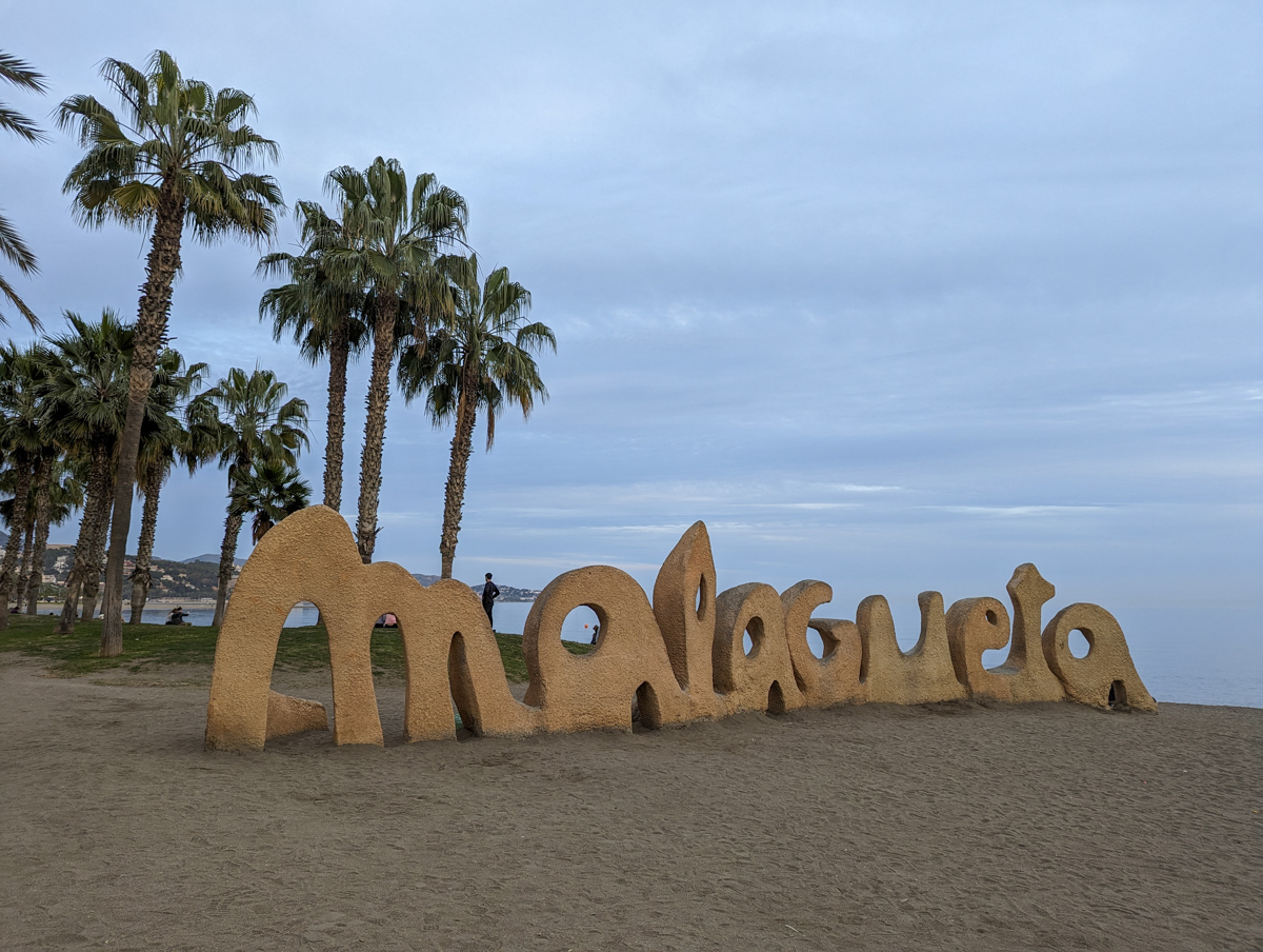Lettering of Malagueta with golden sand and palm trees in the background.