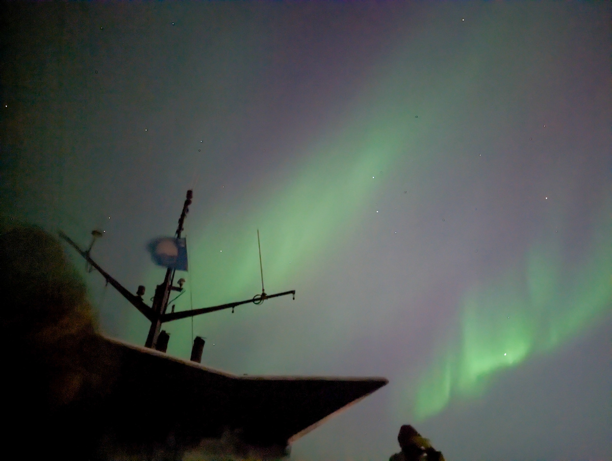 Northern Lights flashing above a boat silhouette in Reykjavik harbour