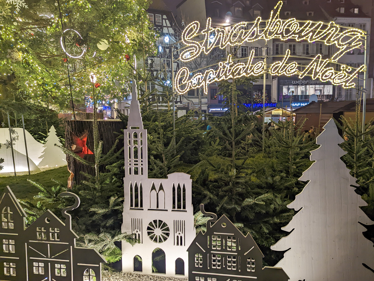 Bright lights of Strasbourg Christmas Market with fir trees in the background.