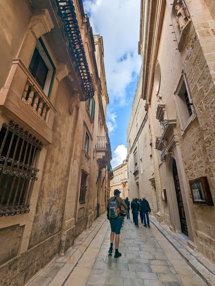 Honey coloured buildings on the streets of Malta and a man walking down them, warm day in Malta in winter.