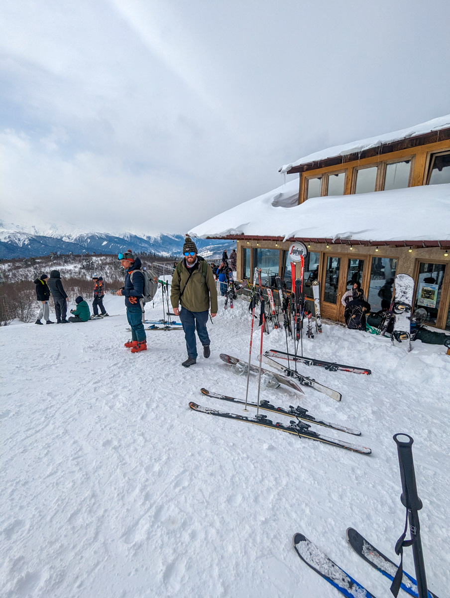 Skiers gathered around a ski lodge with snow-covered mountains in the distance in Mestia, Georgia.