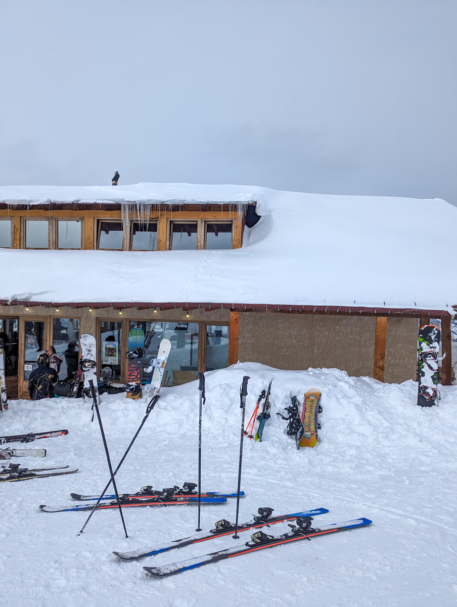 The snow-laden roof of a ski lodge with skis and poles stacked in the snow in the foreground in Mestia, Georgia