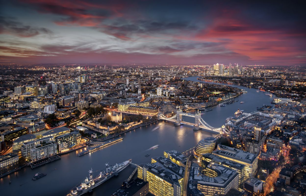 Aerial view of illuminated London, UK, during evening time featuring the Tower Bridge, Thames river and the modern skyscrapers of Canary Wharf