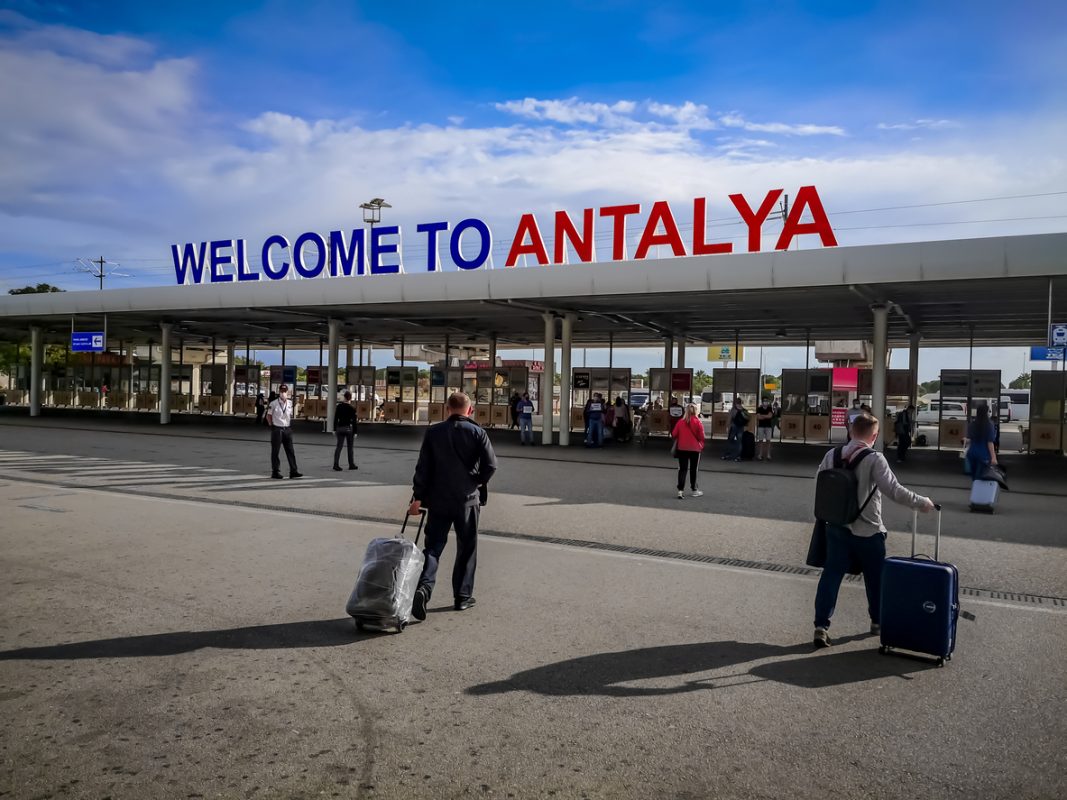 Antalya, Turkey - October 21, 2020: Large signboard Welcome to Antalya at Airport. Tourists with suitcases in the square outside the Antalya Havalimani on a summer sunny day