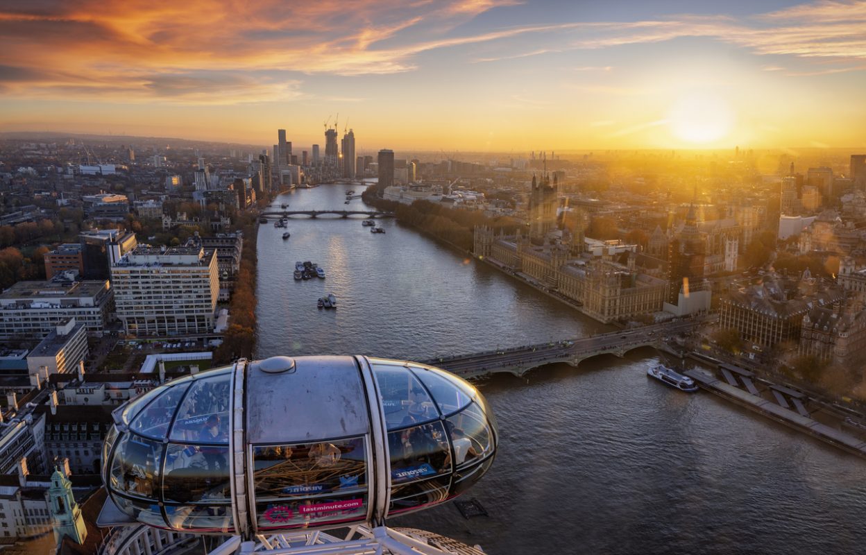 London, UK - November 23rd 2021: beautiful sunset view over the city of Westminster and river Thames from top of the London Eye with a gondola in the foreground and people enjoying the ride
