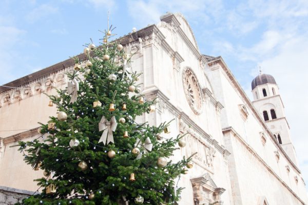 Christmas tree with golden, yellow ornaments, baubles, silver bows in old town with ancient architecture, cathedral, church. Authentic festive atmosphere in streets of Dubrovnik, Croatia