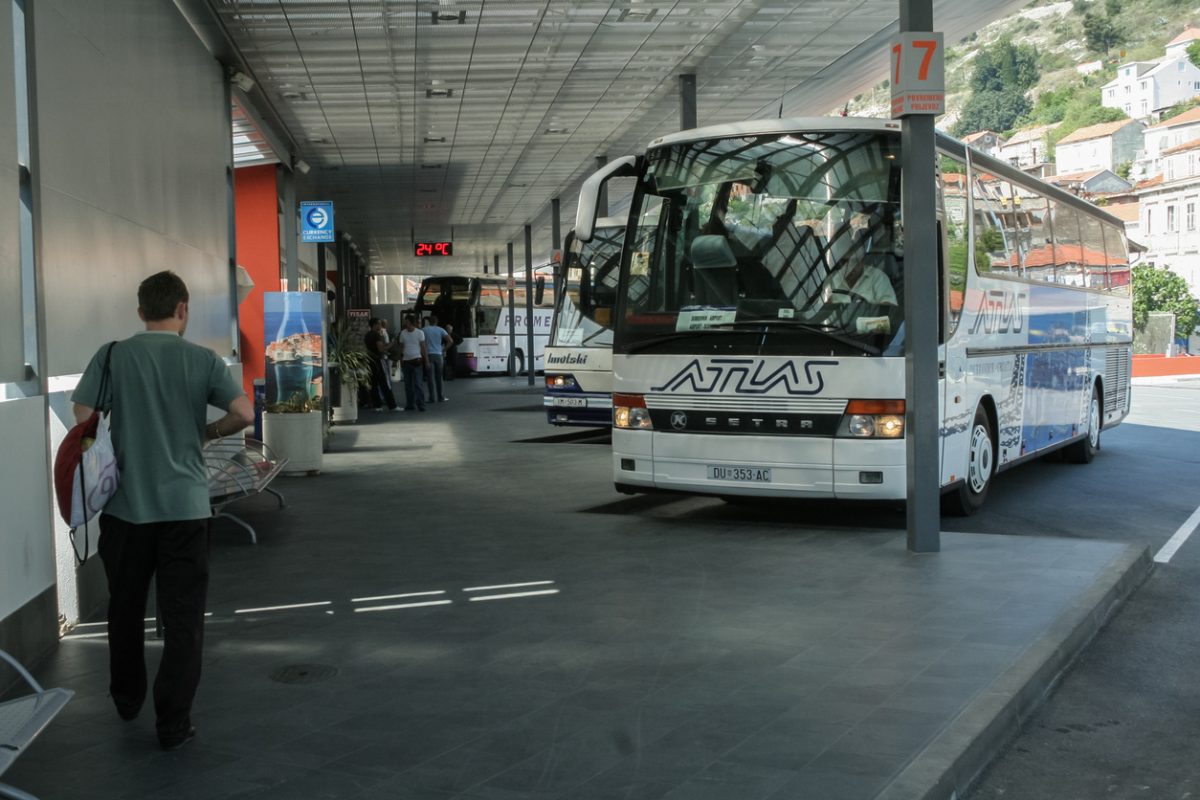Picture of an Atlas Coach ready for departure for a bus service to Dubrovnik airport, on Dubrovnik bus station departure platform and a passenger passing by.