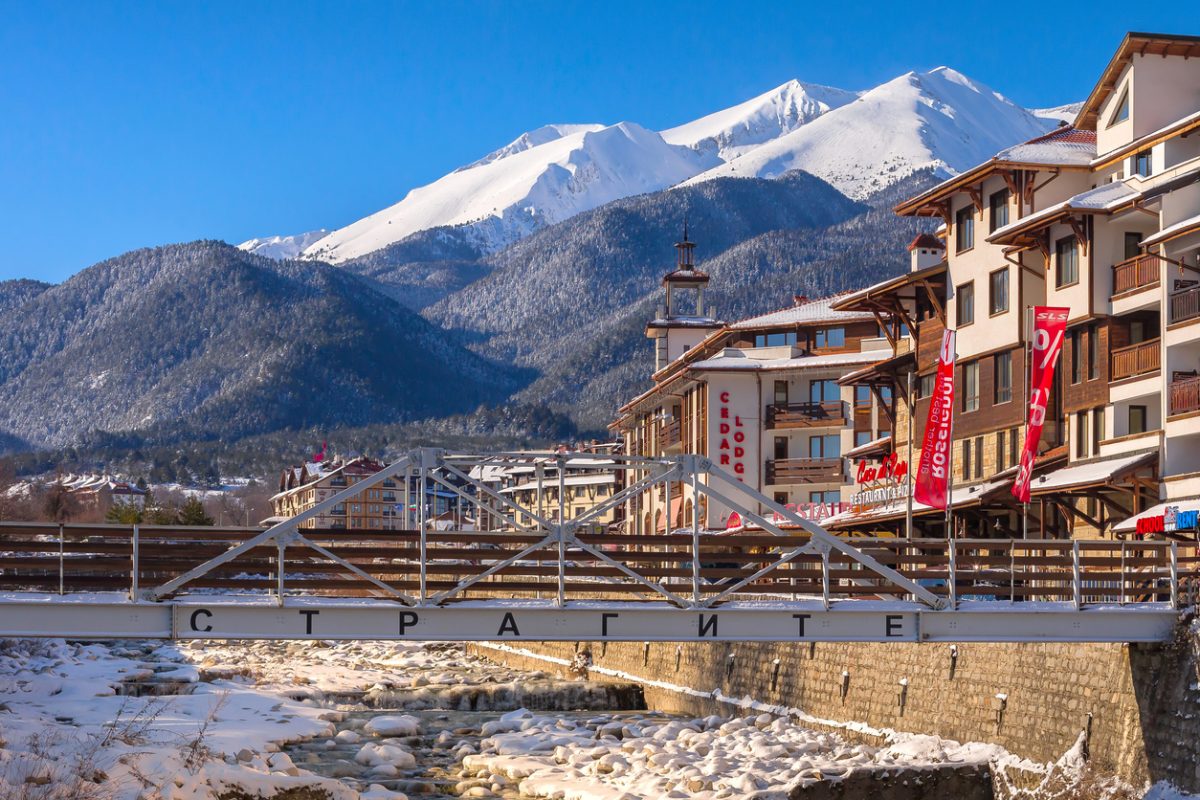 Bansko, Bulgaria - January 28, 2021: Glazne river in bulgarian town, hotel houses and snow Pirin mountains peaks