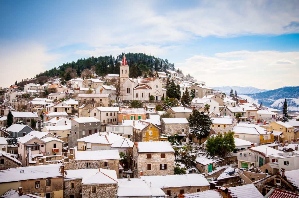 Small Mediterranean town on the slopes of hill with a church on top, covered in snow