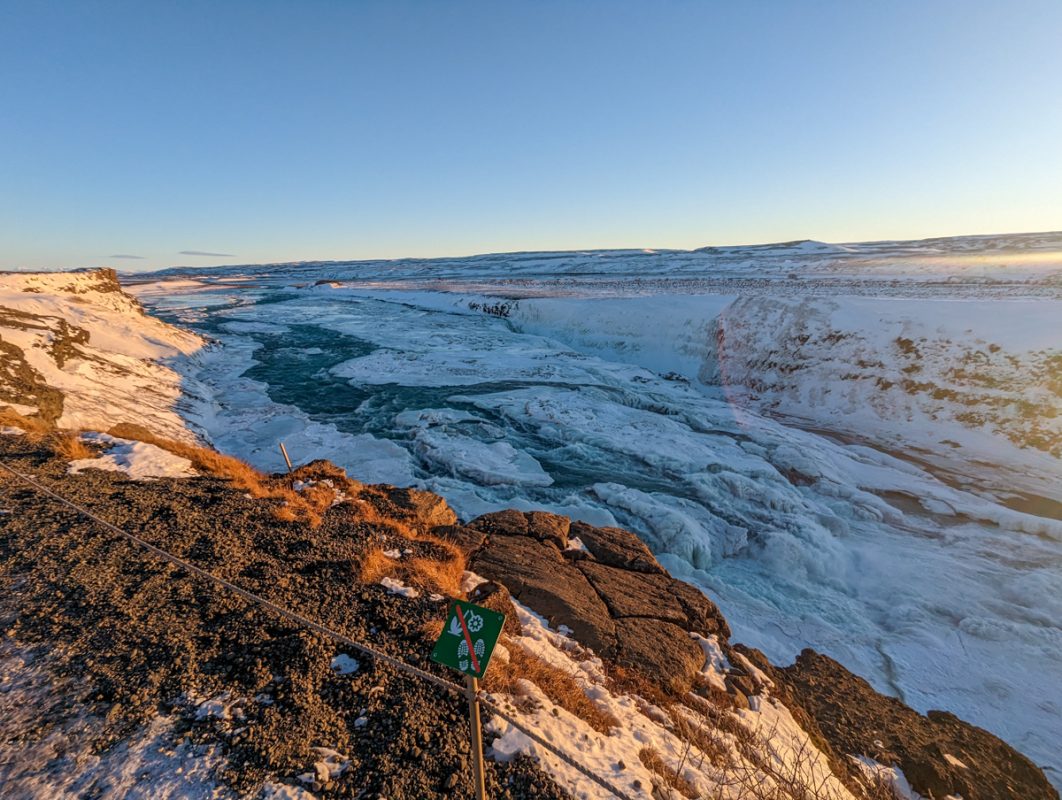 View over Gullfoss Waterfall, a beautiful waterfall that you can view from above in winter. The landscape is snow covered and sun has just risen. 