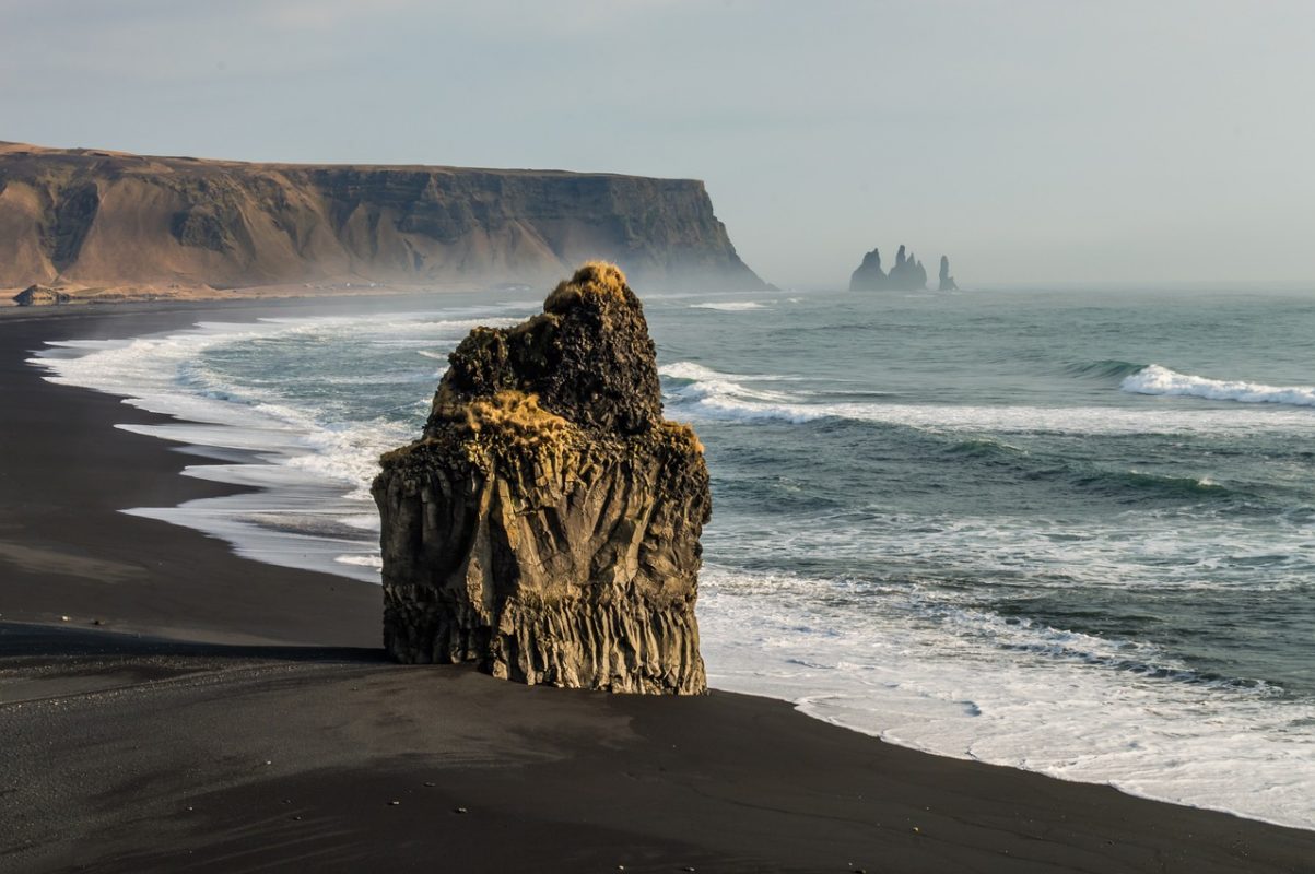 One of Iceland's dramatic black sand beaches with a craggy rock outcrop in the foreground.