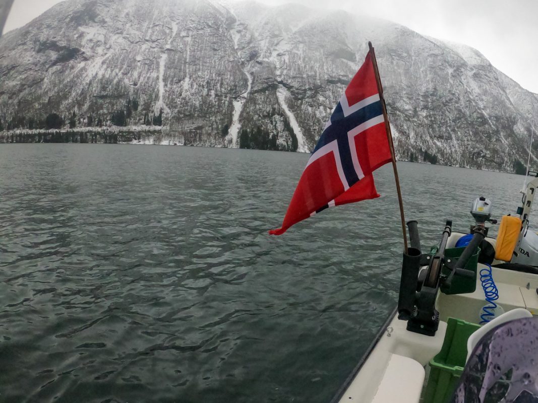 An icy and snowy fjord, with the Norwegian flag in the foreground.