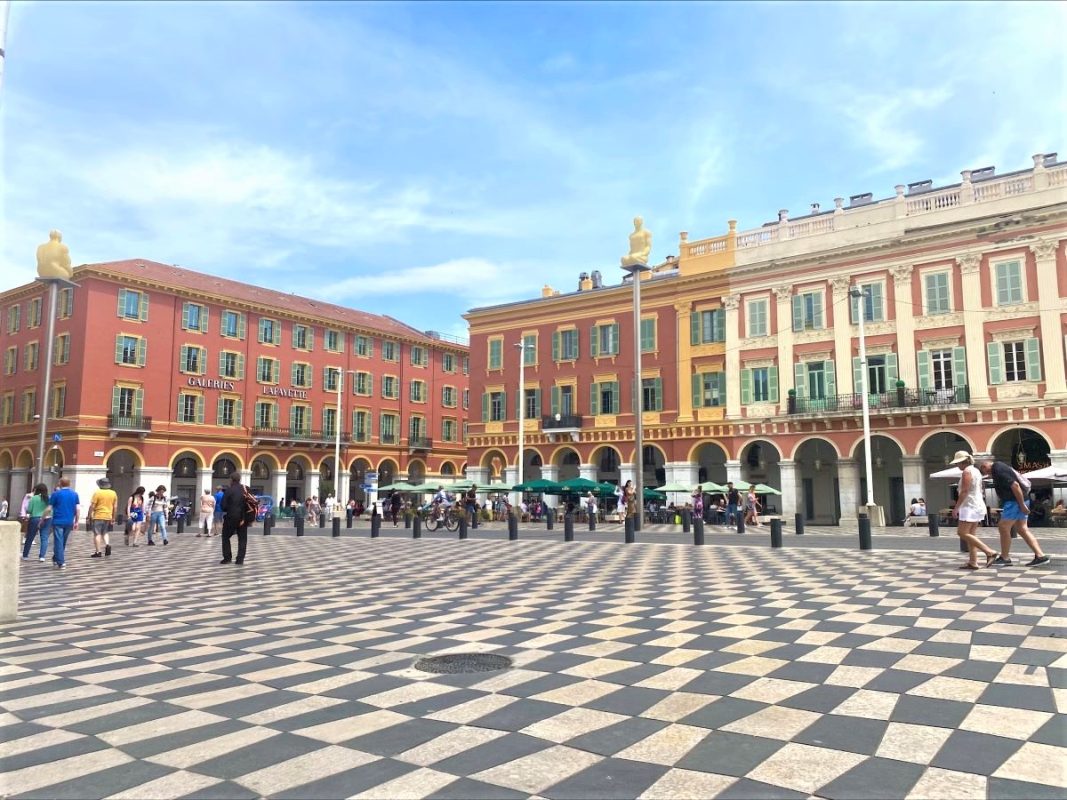 A main square of Nice in France, with black and white tiles and the pink and yellow buildings in the background.
