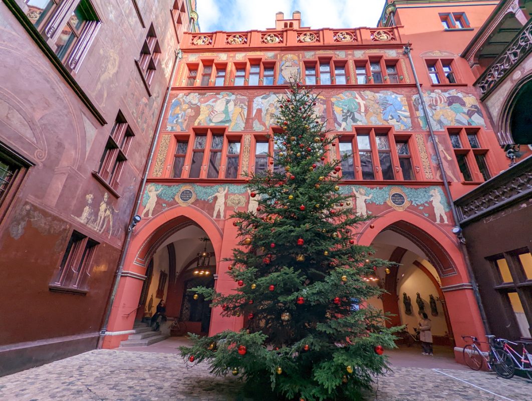 Courtyard of the Basel Minster with a huge Christmas tree inside and paintings on the walls.