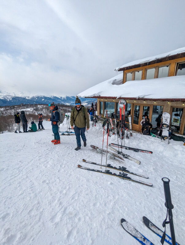 Skiers gathered around a ski lodge with snow-covered mountains in the distance in Mestia, Georgia.