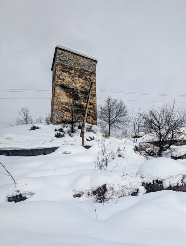 An old stone watchtower characteristic of the Svaneti region, perched on a snowy hill, with a cloudy sky above in Mestia, Georgia.